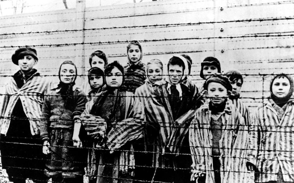 a group of children wearing concentration camp uniforms at the time behind barbed wire fences in the Nazi concentration camp Oswiecim (Auschwitz)