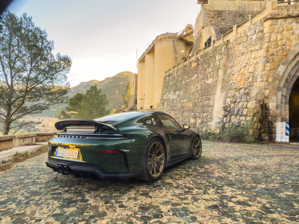 A green Porsche 911 GT3 parked next to what looks like it can be a castle.