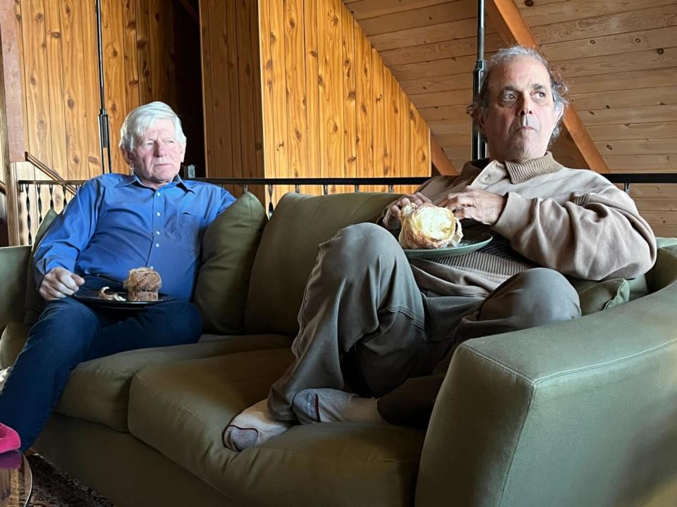 Friends Jack Minckler and Gary Himelfarb sit on a couch and stare to the right.