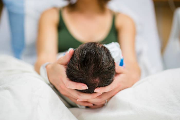 Person gently cradling a newborn's head and demonstrating a caring moment in a hospital setting