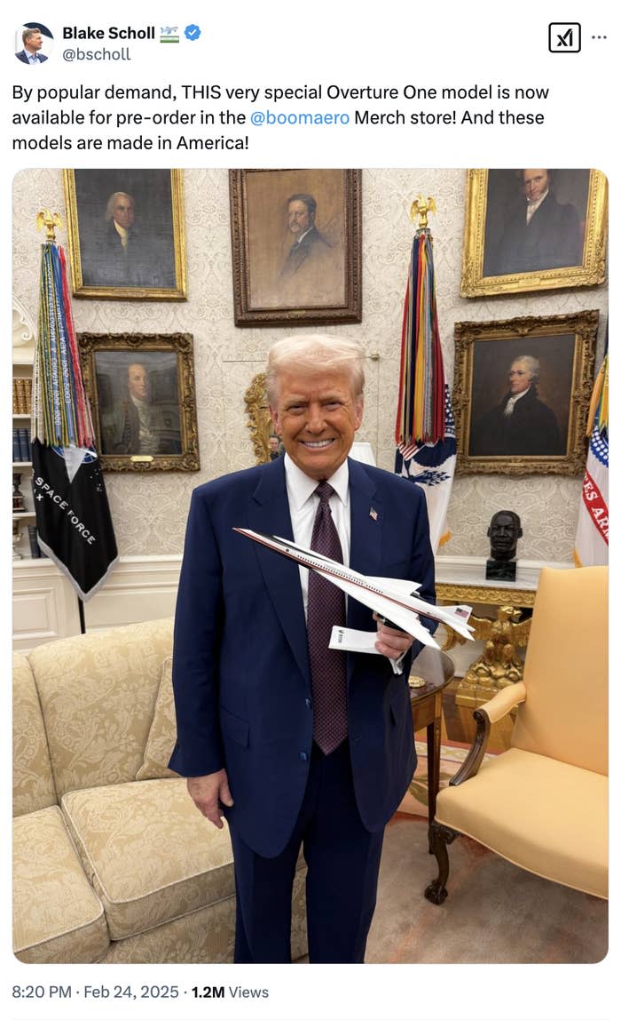 A person in a suit holds a excess one model jet in an office environment, surrounded by historic portraits