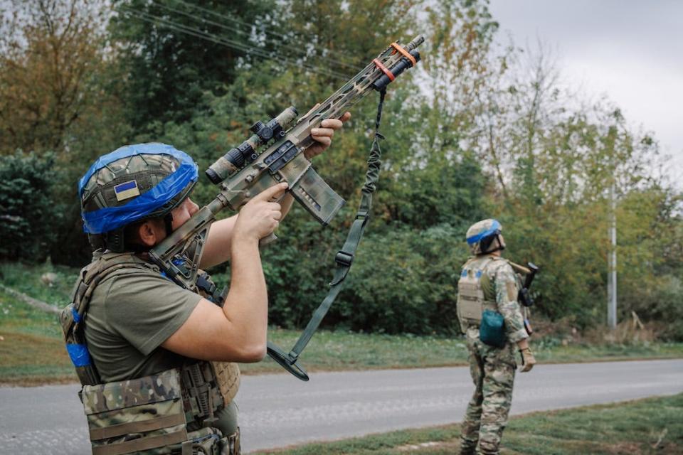 A Ukrainian soldier looks through the scope of a gun, with another soldier nearby.