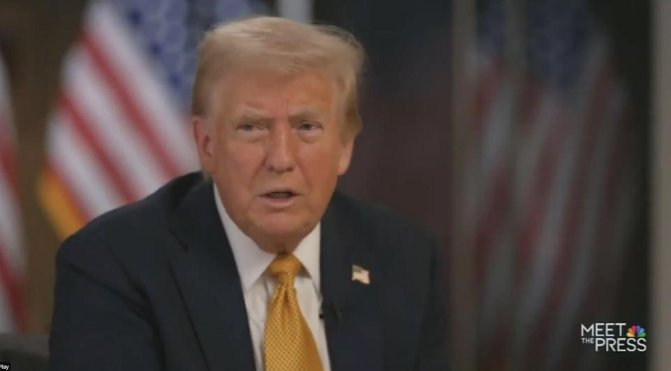 A person in a suit and tie speaks during a "Meet the press" interview. American flags are in the background