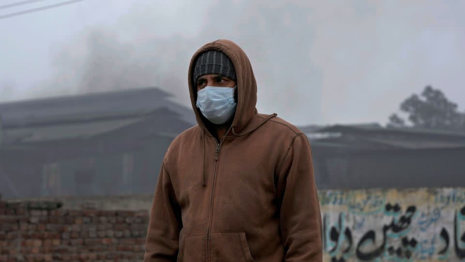 A man is wearing a mask while walking past a small iron factory in Lahore, Pakistan, on January 16, 2024. - KM Chaudary/AP