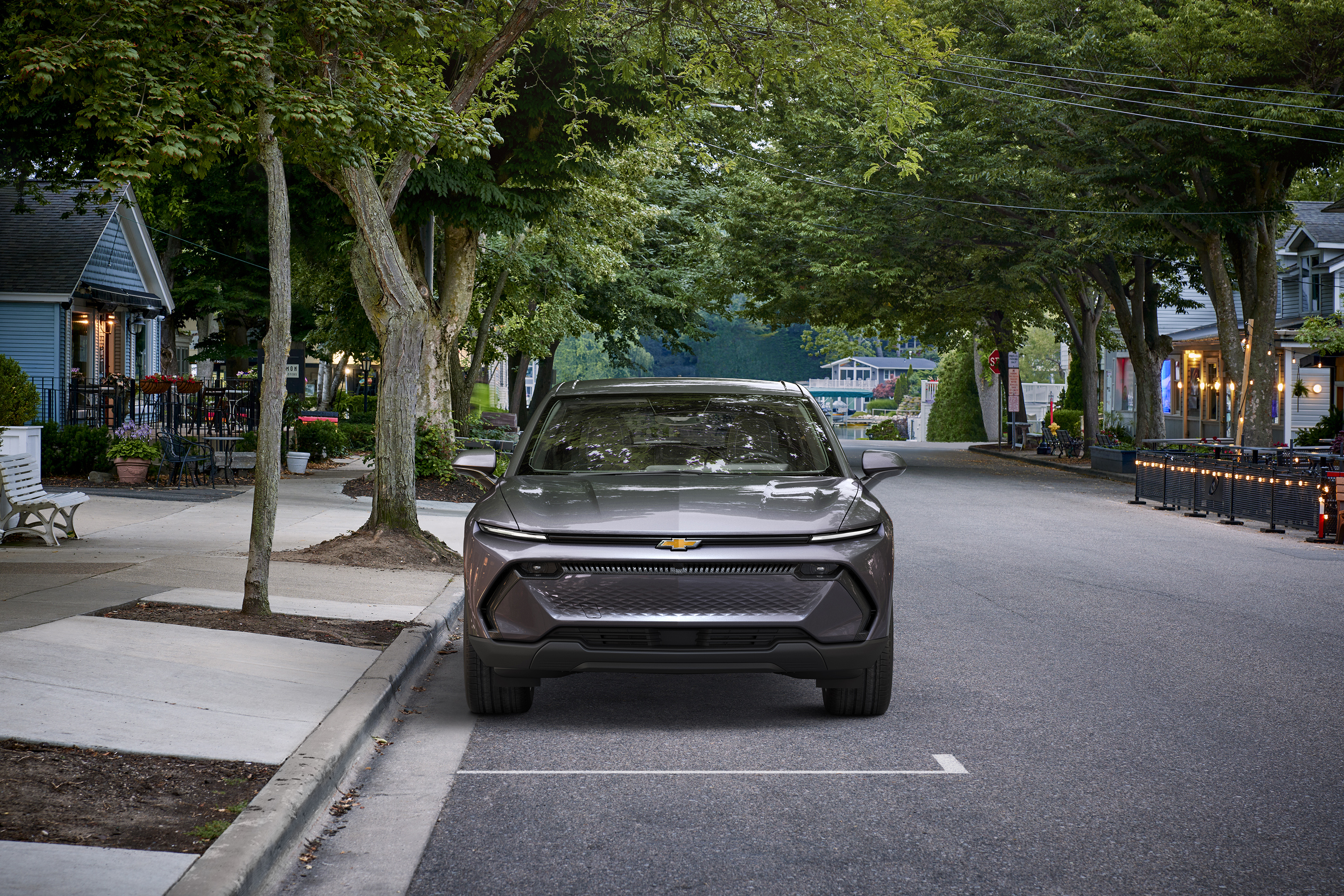 Front view of the 2024 Chevrolet Equinox EV 1LT in Galaxy Gray Metallic parked on a tree-lined street. Pre-production model shown. Actual production model may vary. Visit chevy.com/EquinoxEV for availability.