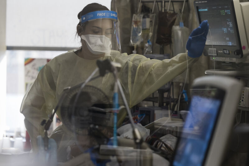 A woman in personal protective equipment operates machines.