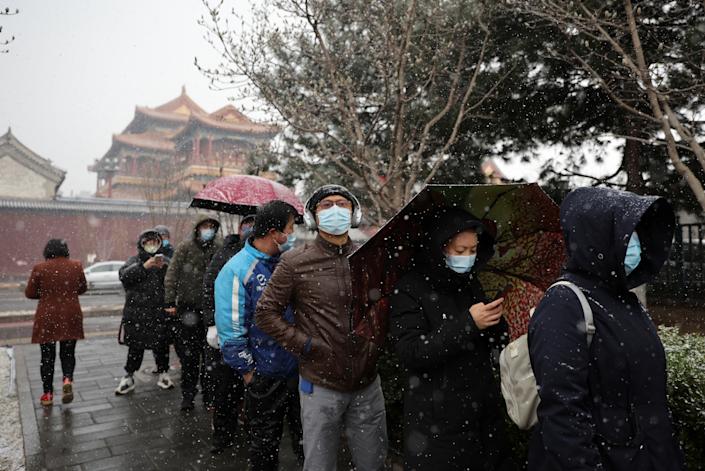 People queue amid snowfall.