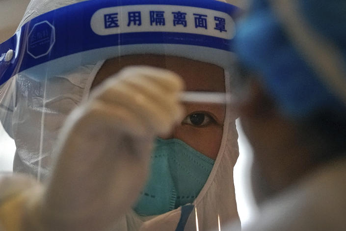 A health worker in a protective suit takes a sample from a throat swab.