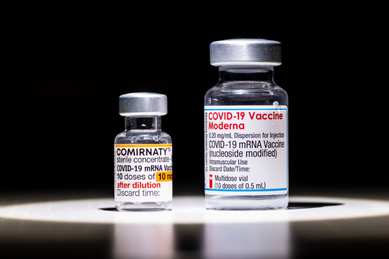 A bottle of COMIRNATY (Pfizer/BioNTech) and a bottle of Moderna COVID-19 vaccines.