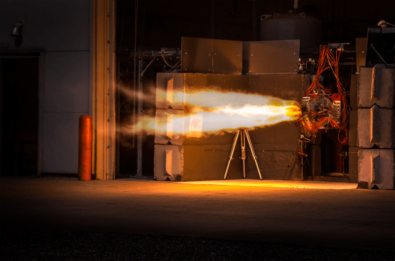 A missile component blows out flames in a darkened warehouse.