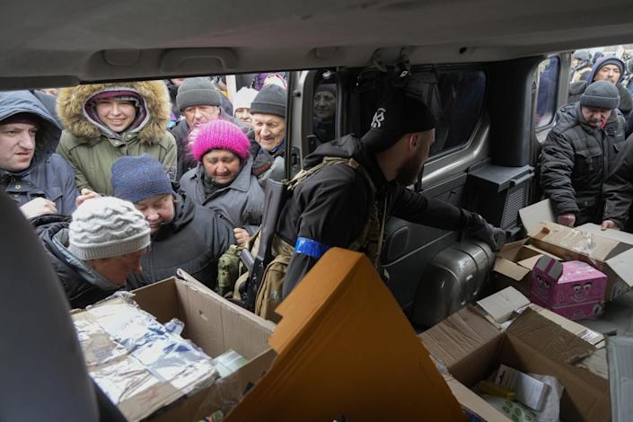 People in winter clothes and knitted hats gather outside the open door of a vehicle with open boxes inside