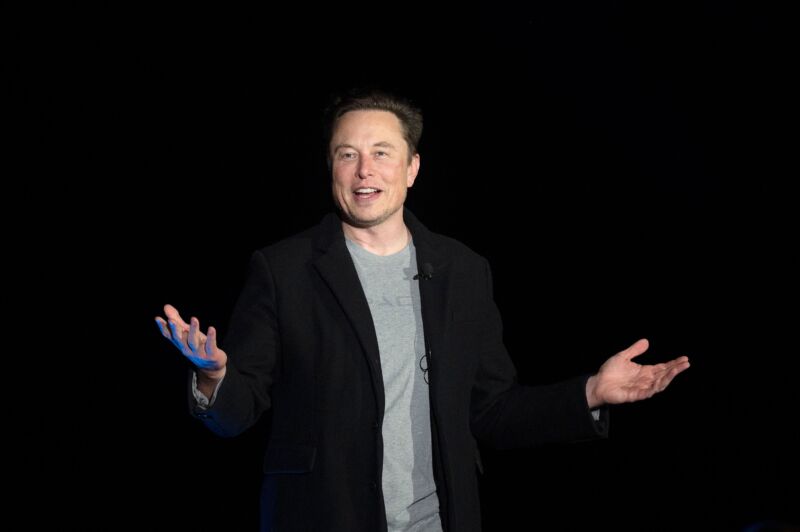 Elon Musk stands and gestures with his hands as he speaks at a press conference.