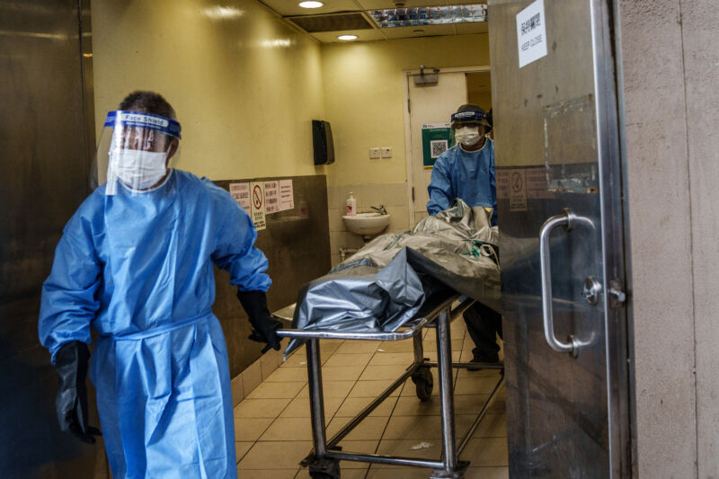 Health workers wearing personal protective equipment transport the body of a deceased patient to a hearse outside the mortuary of Queen Elizabeth Hospital in Hong Kong, China, on Wednesday, March 2, 2022.  Hong Kong reported more than 55,000 cases on Wednesday.  hospitals are under water and the city's morgues are nearly full.