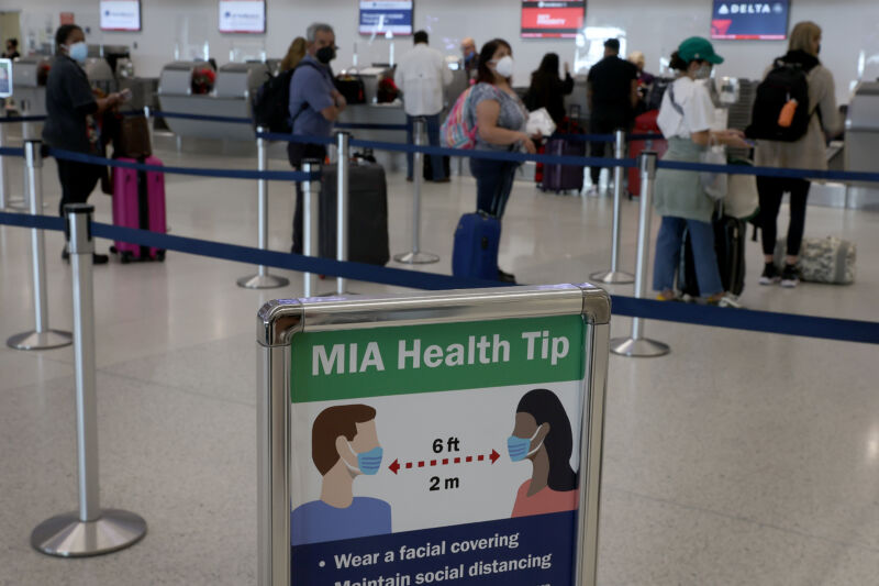 A sign advises people to wear masks and stand six feet apart as travelers make their way through Miami International Airport on Dec. 28, 2021. 