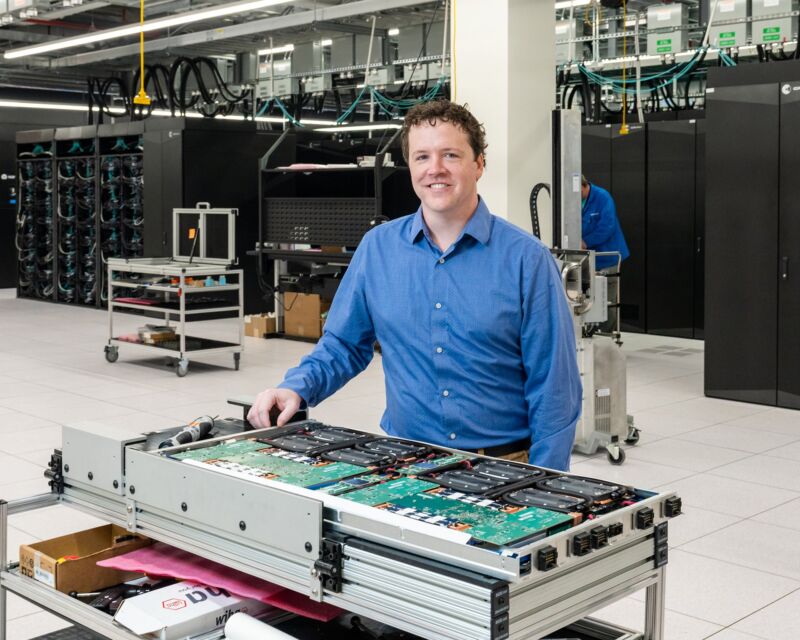 A systems engineer stands in a large room with the Frontier supercomputer.