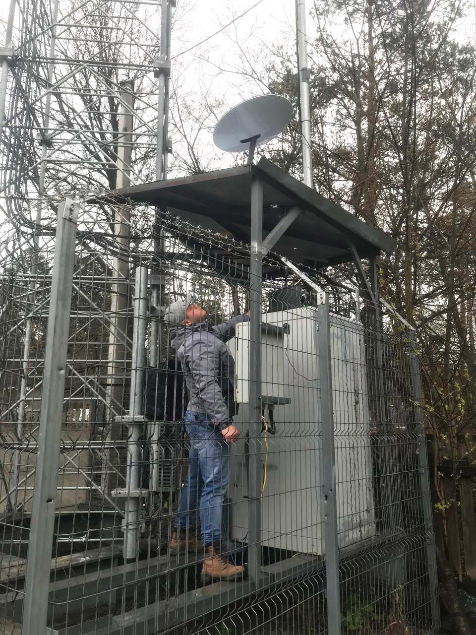 Person standing under Starlink satellite terminals installed on a transmission tower near Irpin, Ukraine.