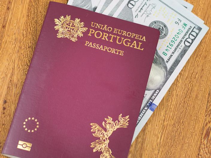 Portuguese passport (translation "European Union Portugal Passport") and hundred dollar banknotes wooden background