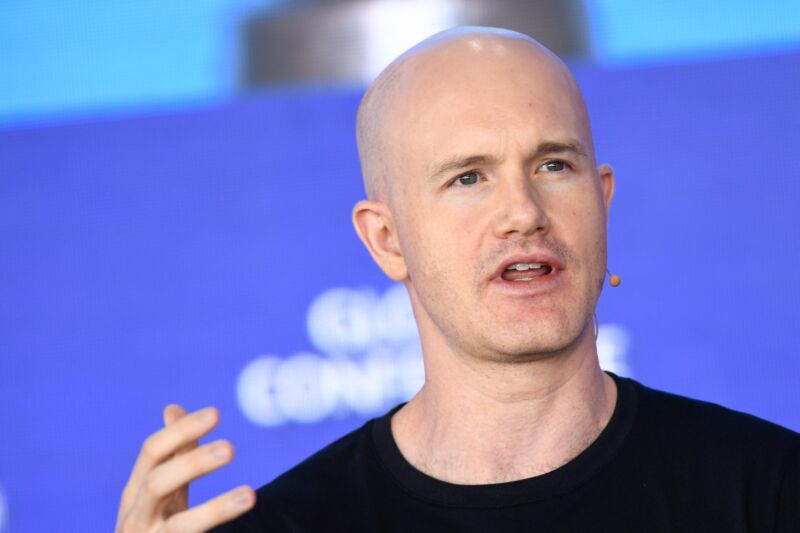 Brian Armstrong, CEO of Coinbase, speaks at a conference and gestures with his hand.