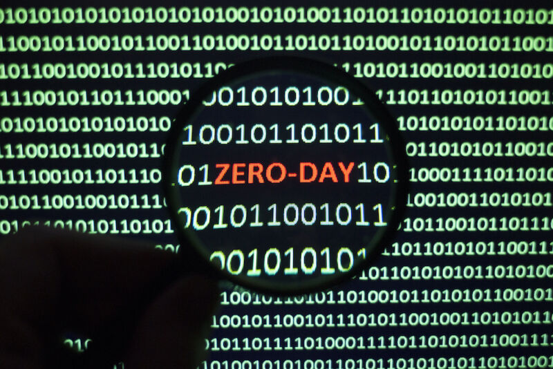 The phrase Zero Day can be seen on a monochrome computer screen that is full of ones and zeros.