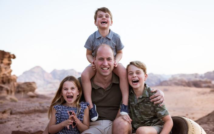 Princes George and Louis and Princess Charlotte are hugged by their father in the newly released photo - The Duke and Duchess of Cambridge