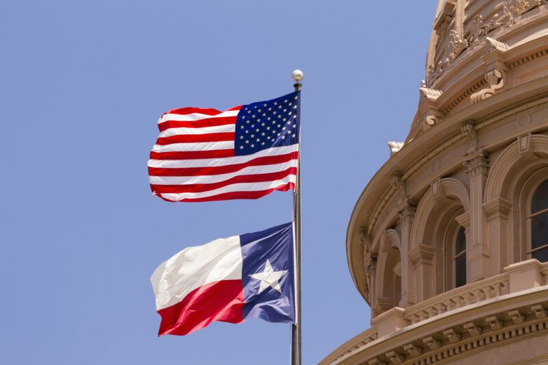 US and Texas flags seen outside the Texas State Capitol Building during the day.