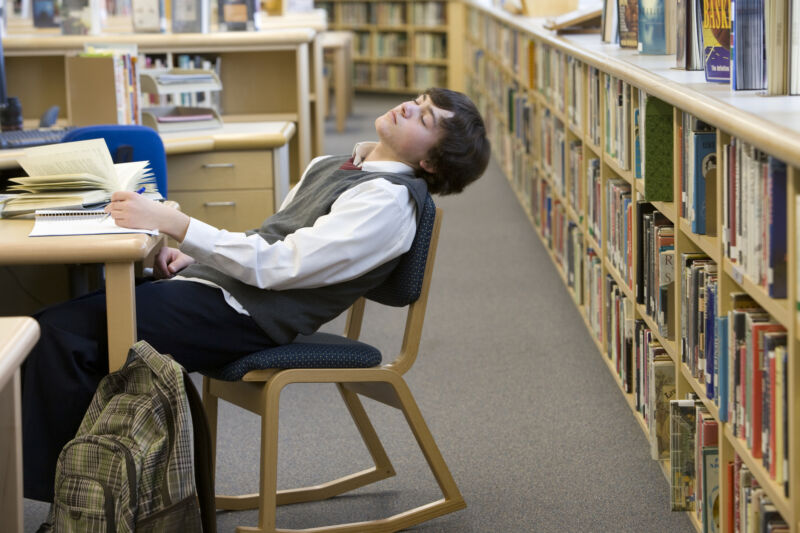 Image of a teenager in a library, slumped in his chair.l