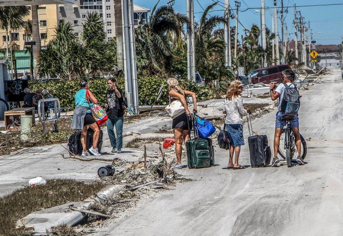 Residents walk with suitcases along Estero Boulevard as they exit Fort Myers Beach and Estero Island, two days after Hurricane Ian hit Florida's west coast as a Category 4 storm.