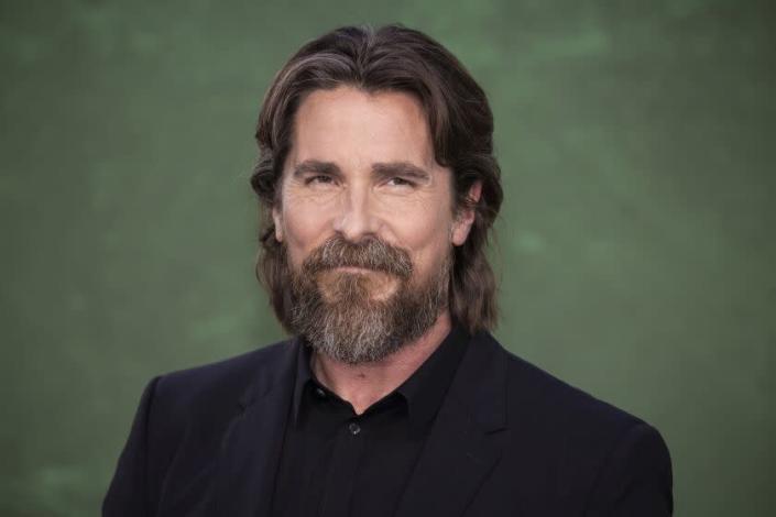 Christian Bale with long hair against a dark green background