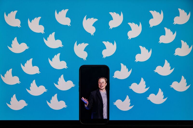 A cell phone with a picture of Elon Musk on a computer screen covered with Twitter logos.