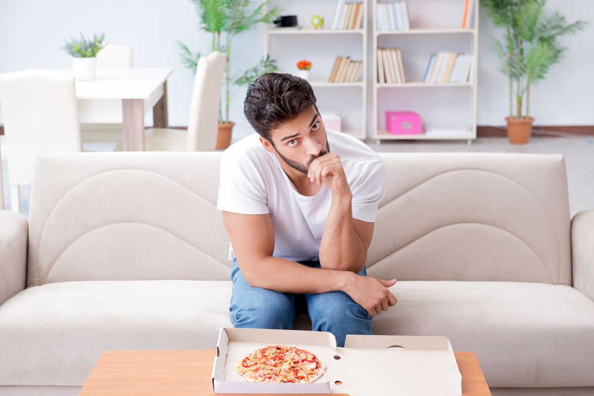 Man in the living room thinking about his pizza on the table