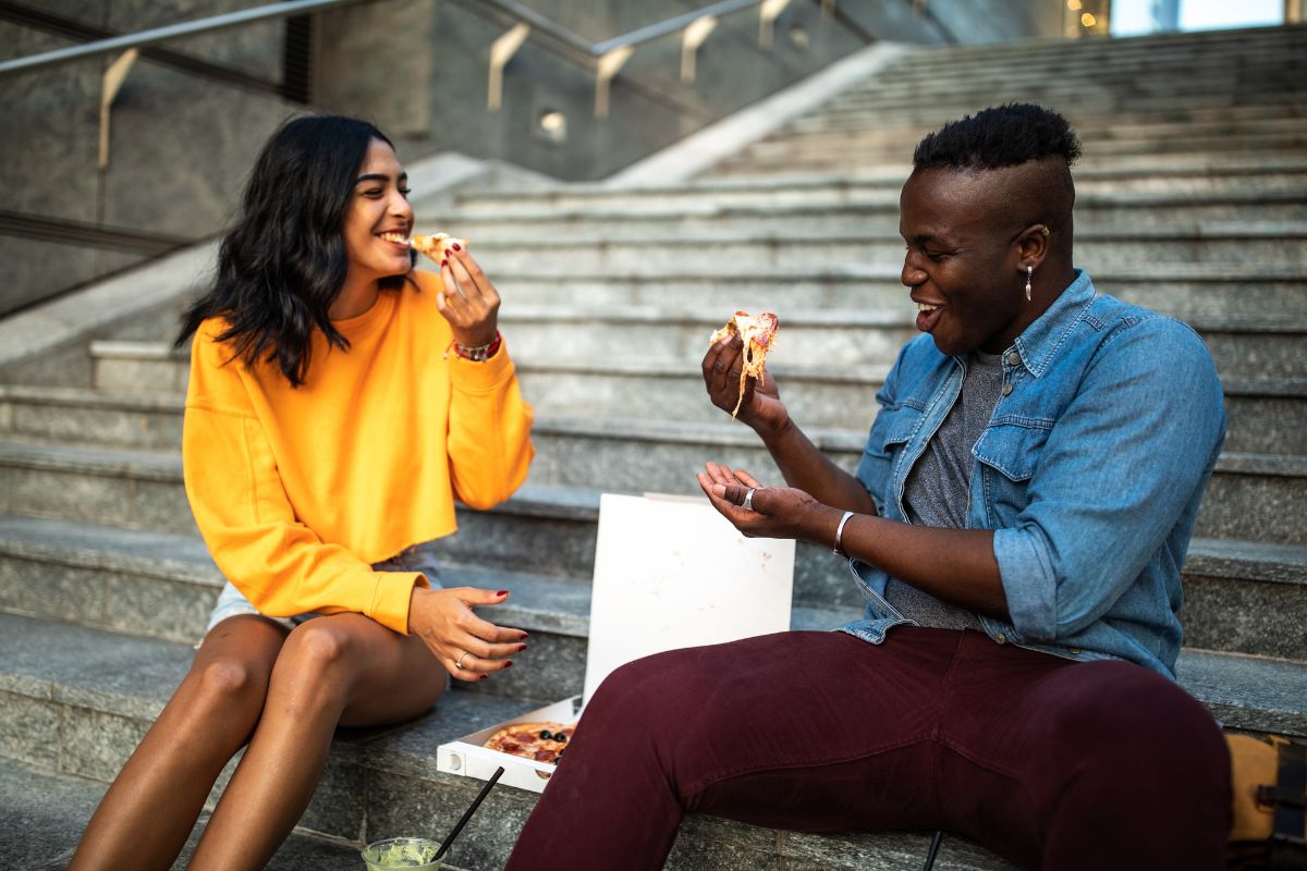 a woman and a man eat pizza on the stairs