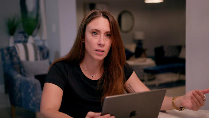 Casey Anthony in a black T-shirt looks a little off-camera in front of an iPad.  she gestures with her left hand, palm up.  (Peacock / NBC Universal)