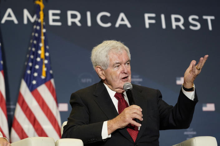 Former House Speaker Newt Gingrich sits on stage and speaks into a microphone during an America First Policy Institute summit in Washington.