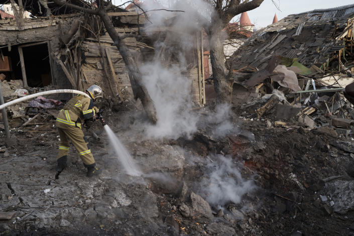 A firefighter aims a high-powered fire hose at a blaze next to homes destroyed in a Russian attack.