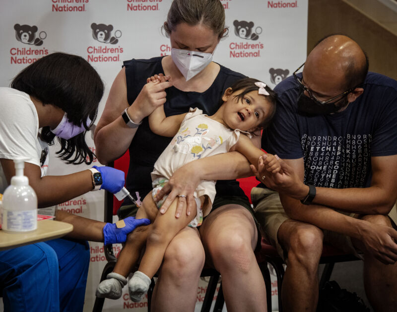 Reisa Lancaster RN, left, administers the Covid-19 vaccine to 14-month-old Ada Hedge, center, comforted by mother Sarah Close and father Chinmay Hedge, right at the Children's National Research and Innovation Campus in Washington, DC. 