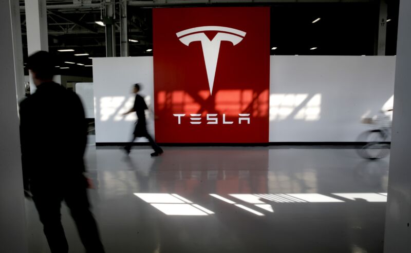 Employees walk past a large Tesla logo.