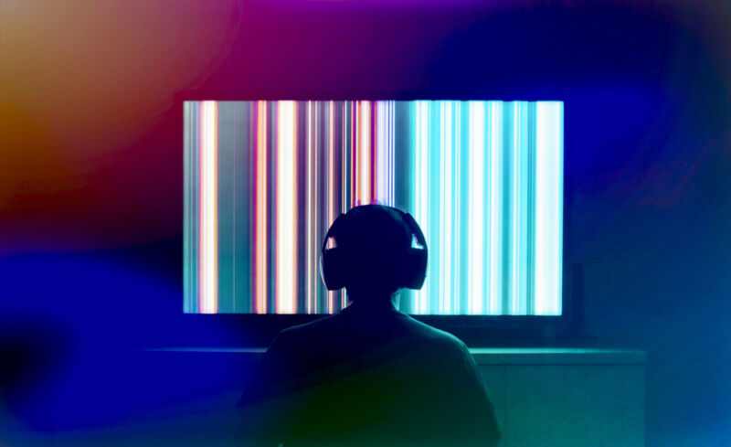 Silhouetted person looking at a large OLED screen with headphones