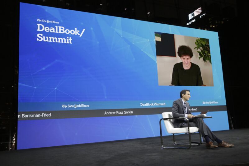 Journalist Andrew Ross Sorkin sits on stage at a conference as he interviews Sam Bankman-Fried, who appeared from a distance and was seen on a giant video screen.