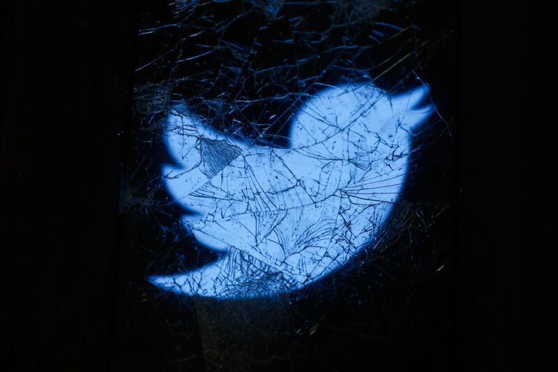 The Twitter logo displayed on a cracked phone screen can be seen through broken glass