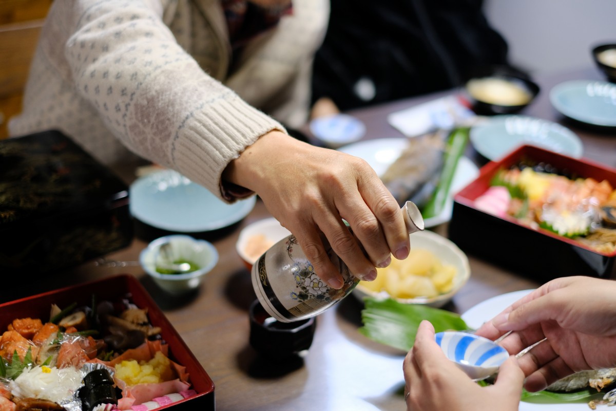 Hand with bottle pouring sake into a cup