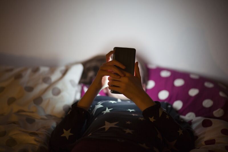 Girl lying on bed at night and using mobile phone