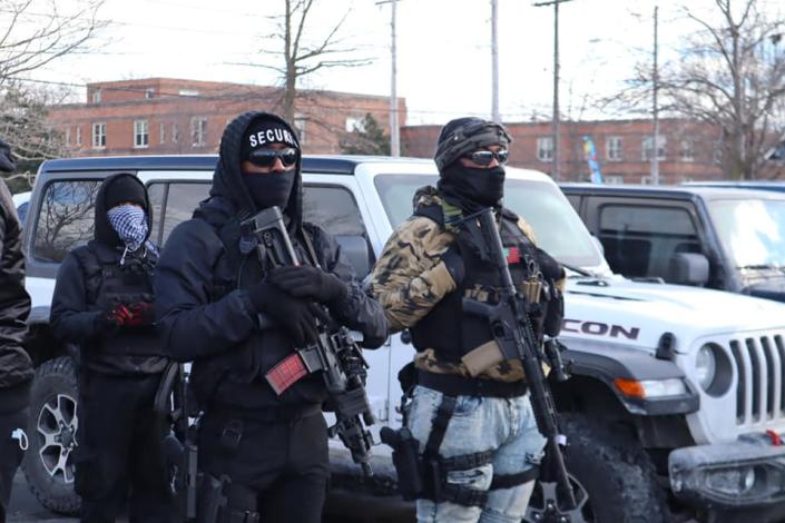 In dark glasses with masks and woolen hats, and guns in hand, New Era members stand guard on a city street.