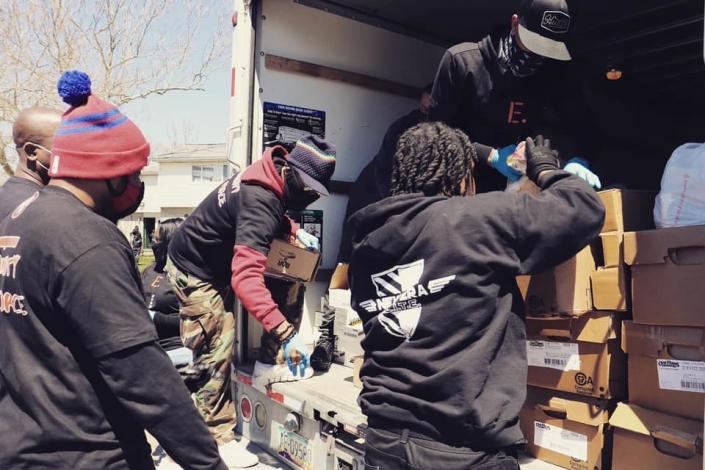 Four members of New Era Detroit gather behind a truck while another passes boxes of food to give to senior citizens.