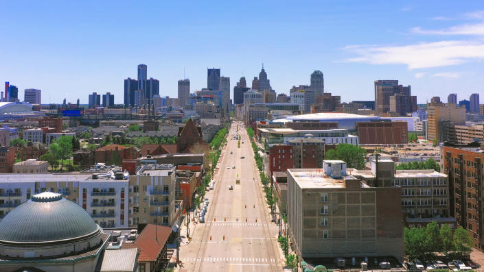 An aerial view of Detroit, with wide, empty Woodward Avenue and tall buildings in the distance.