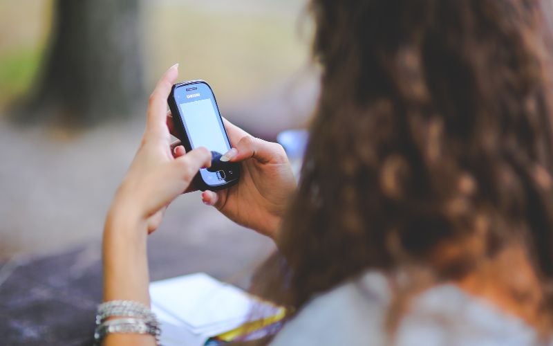 Woman looking at the screen of a mobile phone from behind