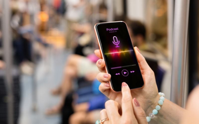 A woman's hands with a bracelet accessing a podcast on a smartphone