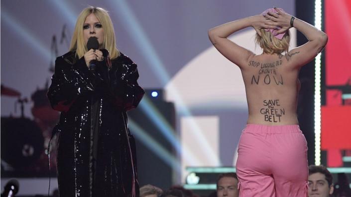 Avril Lavigne on stage at the Juno Awards, next to a topless environmental activist