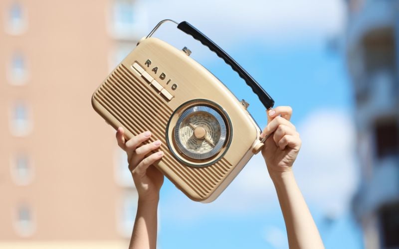 Two hands hold up a small beige portable radio