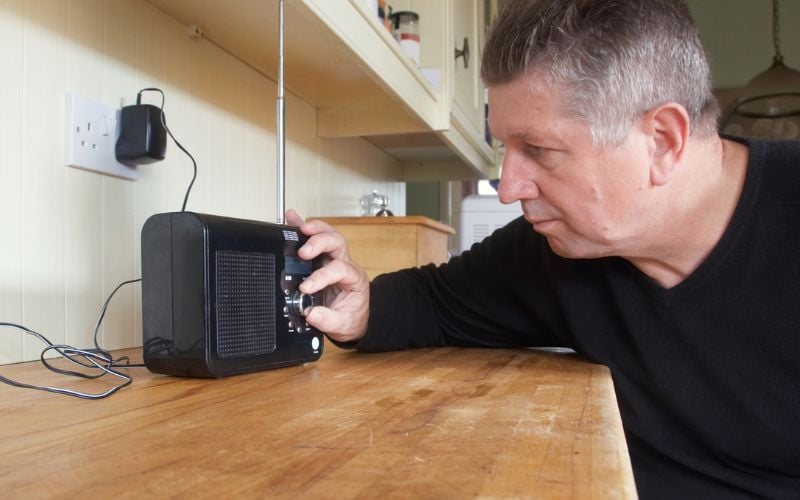 Gray haired man in black shirt tuning in to DAB radio reception on wooden countertop