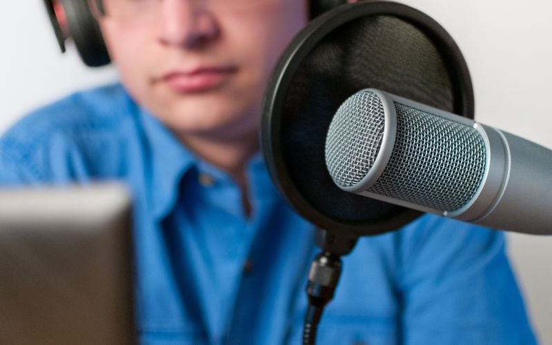 Radio broadcaster with headphones and blue button down shirt with microphone and open laptop;  The man is blurred